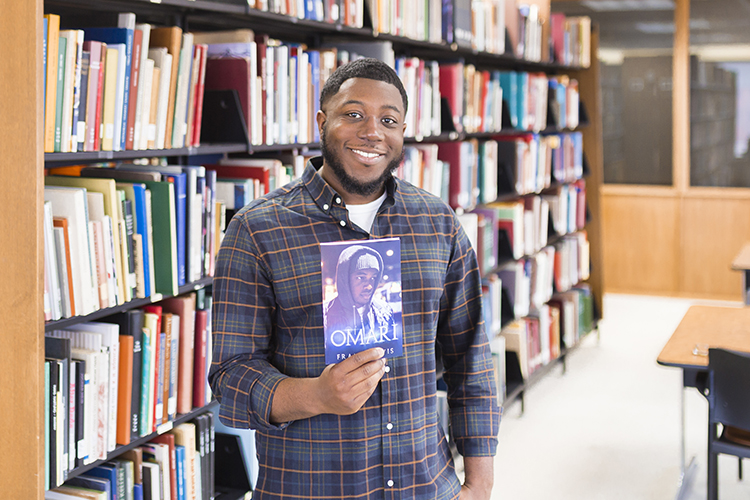 Frank Lewis holds up his book as he poses in a library.