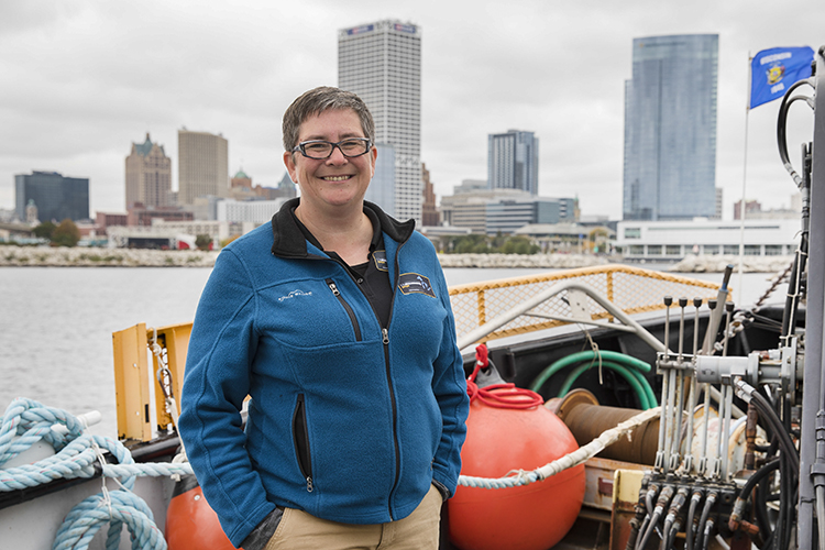 A woman stands aboard a ship on Lake Michigan with the Milwaukee skyline behind her.