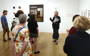 A woman stands in an art gallery talking to several visitors.
