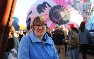 A woman stands in front of two hot-air balloons.