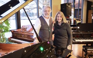 A man and woman stand near a grand piano.