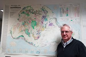 A man stands next to a map attached to a wall. 