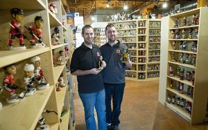 Two men stand in a room full of shelves filled with bobbleheads.