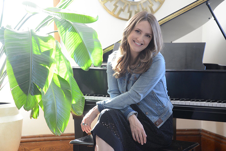 A woman poses in front of a piano.