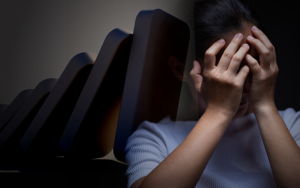 Person with face in hands against a background of falling dominoes