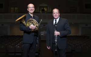 Two UWM professors standing in concert hall holding their musical instruments (French horn and clarinet)