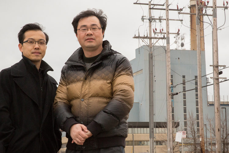 Researchers Wei Wei and Lingfeng Wang stand in front of a power plant.