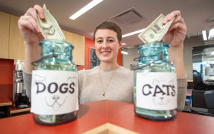 Woman holds a dollar bill in each hand above tip jars on a counter.