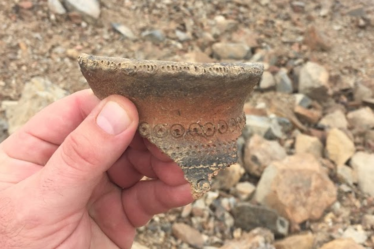A hand holds a broken piece of pottery.