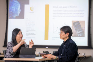 UWM professors Iris Chi and Wonchan Choi discuss their work to reimagine digital libraries in front of a display screen.