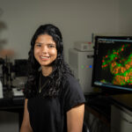PhD student Gabby Voit smiling and sitting in front of lab equipment