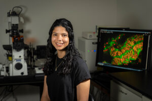 PhD student Gabby Voit smiling and sitting in front of lab equipment