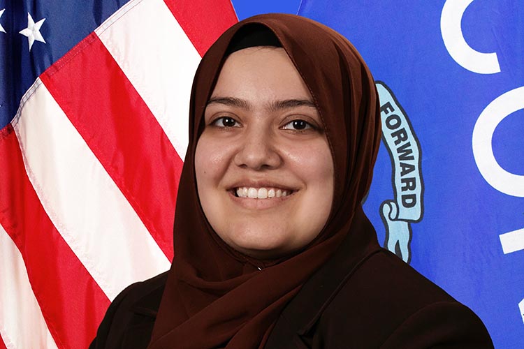 A woman poses for a photo in front of the flags of the U.S. and Wisconsin.