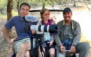 Three people sit next to each other with a large camera in front of them.