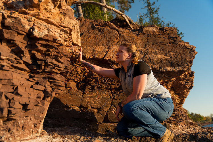 Alum Libby Ives places her hand on layers of ancient rock in Marquette, Michigan.