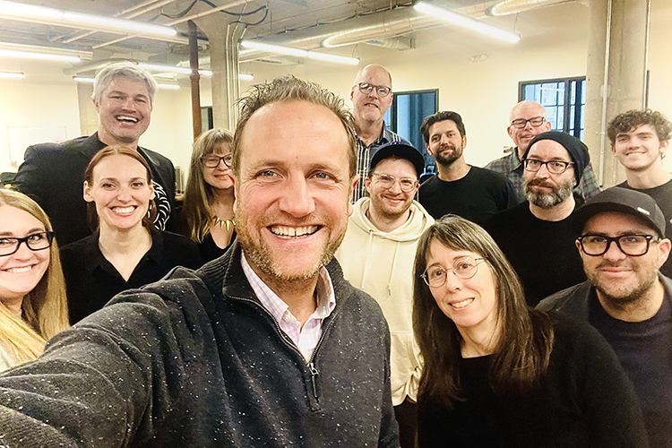 A group of people smile for a selfie in a large room with yellow walls 