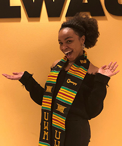 Carrie Mahone holds her arms akimbo while wearing graduation garments 