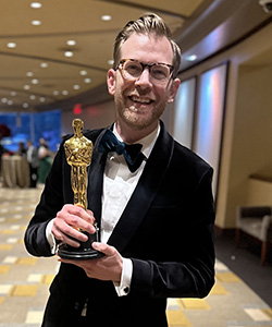 Josh Rosenberg wears a tuxedo and holds an Academy Award 