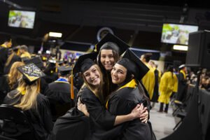 Three women in commencement regalia hug