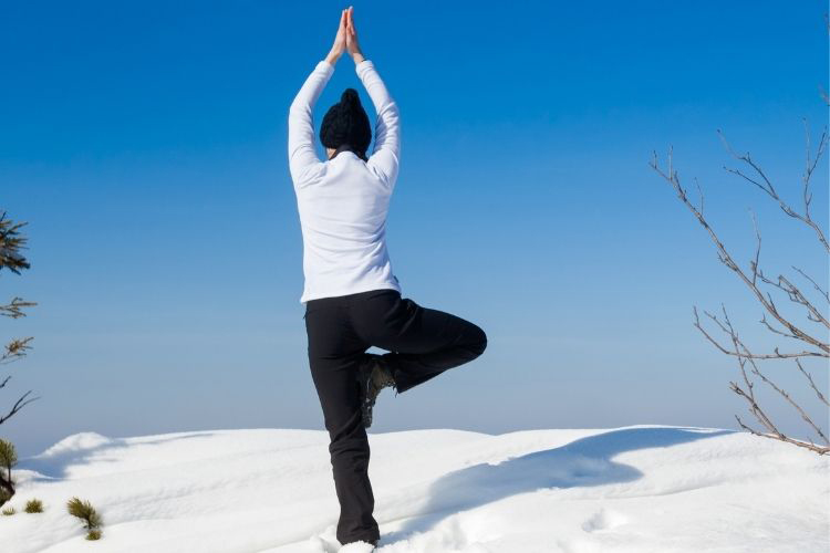 A person is standing in a yoga pose in a snowy spot outdoors