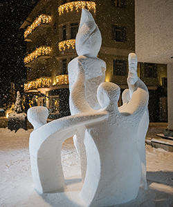 A snow sculpture shows three figures holding an Olympic torch and laurel wreath.