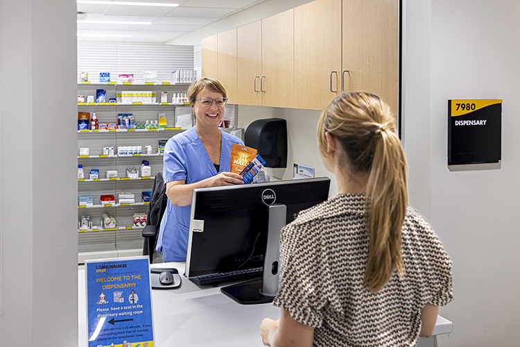 A medical provider in a pharmacy talks with a student patient.