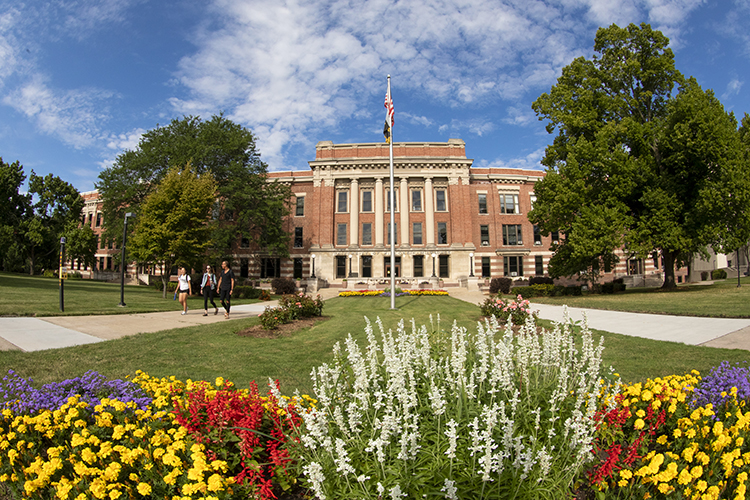 A view of the UW-Milwaukee campus, with flowers blooming in the foreground and a building in the background.