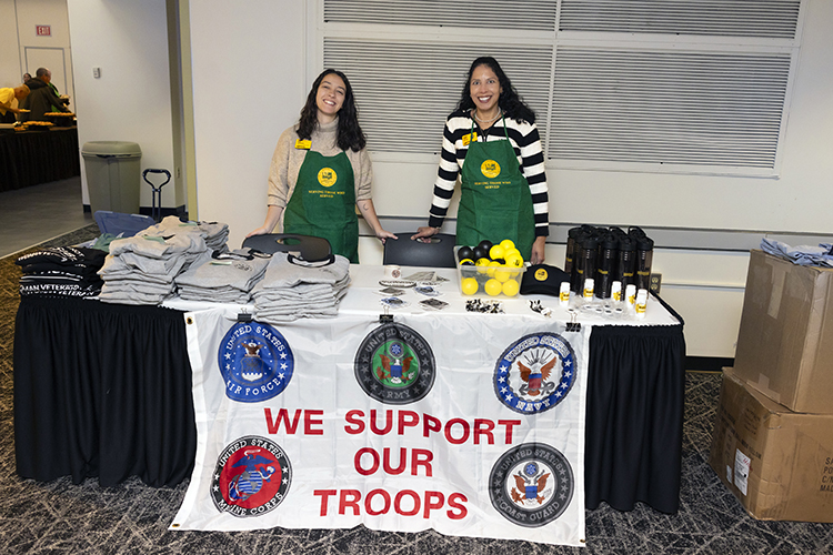 Two women stand at a table with a sign saying "we support our troops"