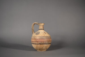 A tan wine vessel with a spherical bottom and looping handle sits on a table. 