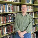 A woman stands in front of a library shelf full of books.