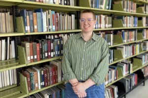 A woman stands in front of a library shelf full of books.