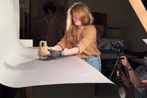 A woman wearing gloves sets an ancient wine bottle on a table. 