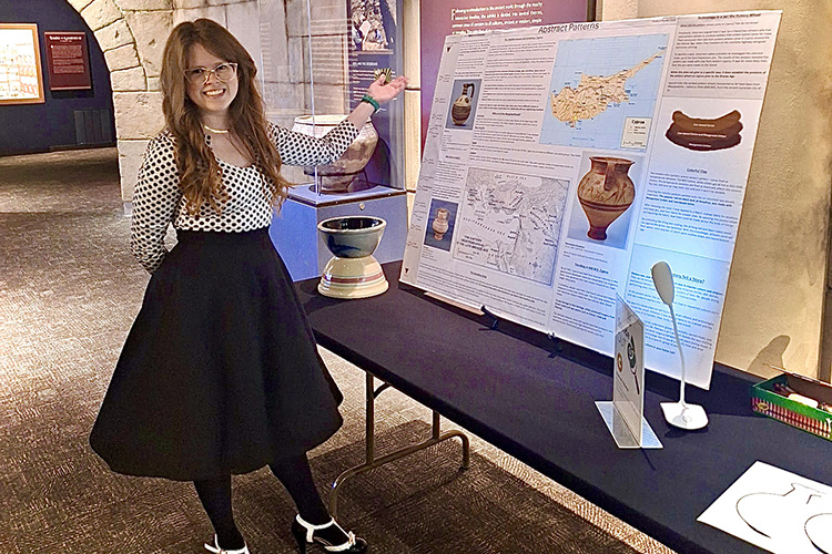 A woman stands in front of a posterboard set up on a table.