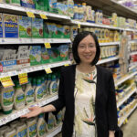 A woman stands in a grocery store aisle in the salad dressing section.
