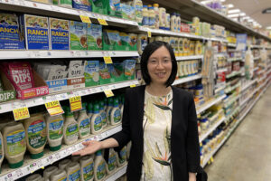 A woman stands in a grocery store aisle in the salad dressing section.
