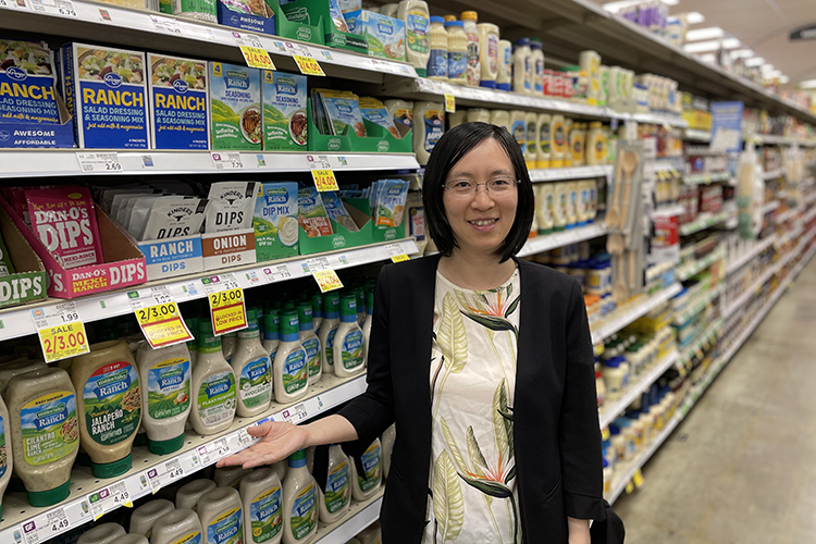 A woman stands in a grocery store aisle in the salad dressing section.