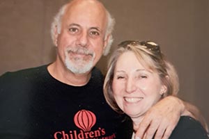 A man and woman stand together, with the man having his arm around her.