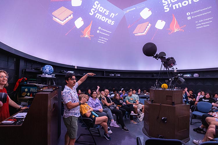 A few dozen people sit in a planetarium, where images of stars and s'mores are projected on the domed ceiling.