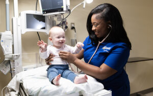A woman in a nurse's uniform listens to a baby's heart with a stethoscope