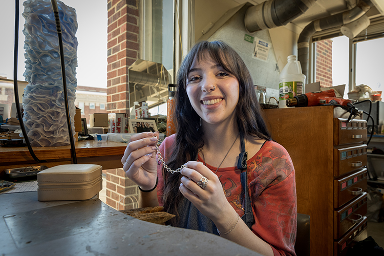 Grace Barden sits at a workbench holding a small chain