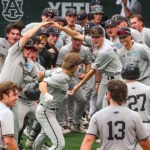 Several baseball players raise their hands in celebration and give low-fives to another player as he approaches the dugout.