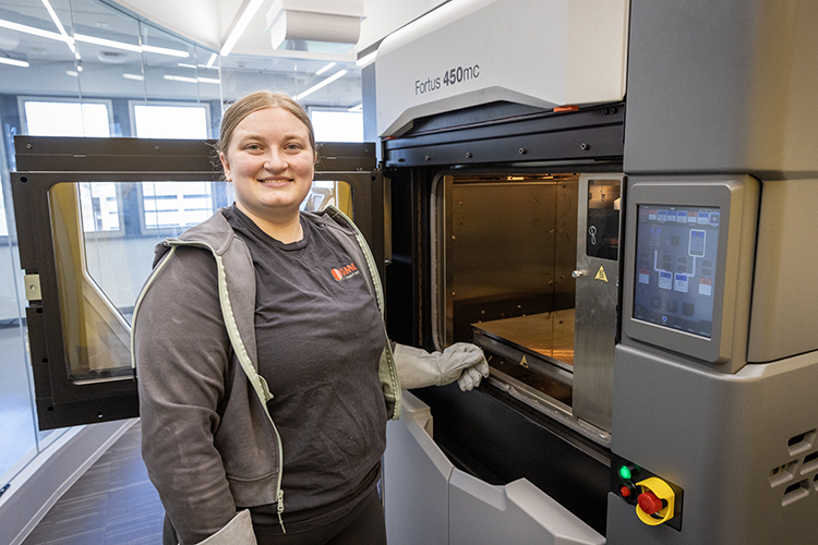 Suzanne Gorman stands at the open door of some industrial equipment while wearing protective gloves