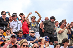 A woman puts her hands in the air to cheer, surrounded by other fans.