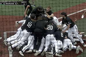 Several people in baseball uniforms jump on top of each other in celebration.