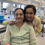 A woman puts her hands on the shoulders of her mother, who sits in a chair in a lab.