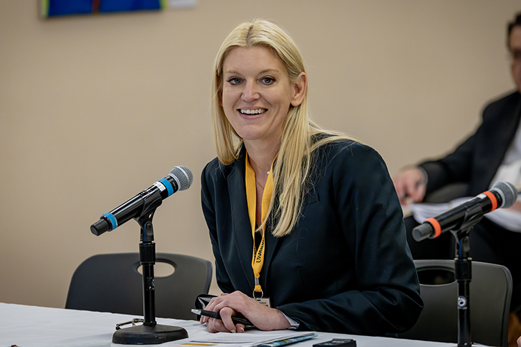 A woman smiles as she sits in front of a microphone at a table.
