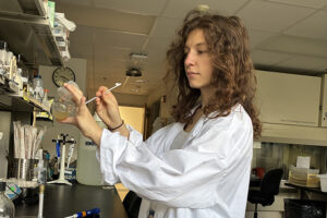 A woman in a white lab coat works with liquid in a beaker in a lab.