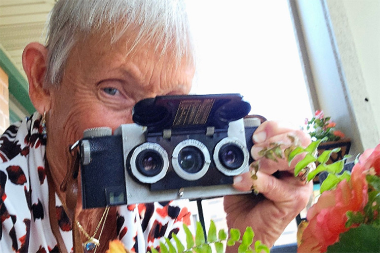A woman hides her face behind a camera with three lenses