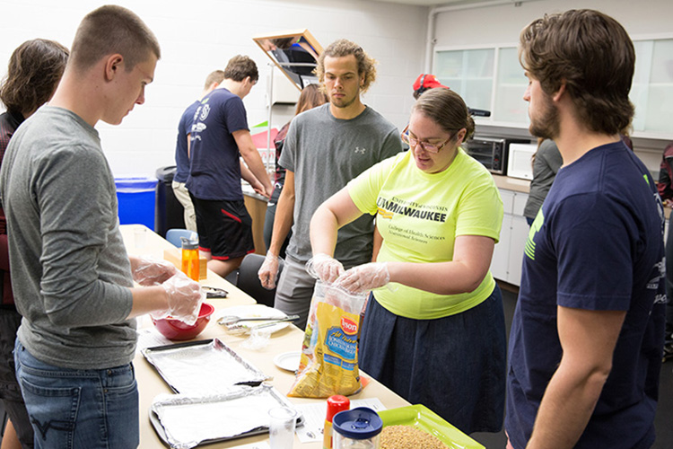 Senior Nutritional Sciences student Crystal Sciarini demonstrates the technique for making "Mock Fried Chicken," a lower-fat version of the popular favorite. Sciarini is one of several UWM students helping teach Junior Olympians how to create healthy meals to fuel their athletic performance. (UWM Photo/Troye Fox)