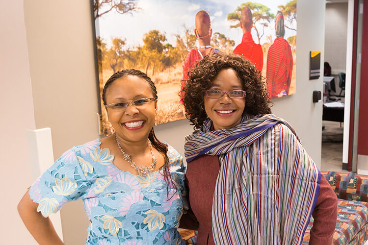 Pennie Kako and Lucy Mkandawire-Valhmu posing in front of a photo in UWM Cunningham Hall